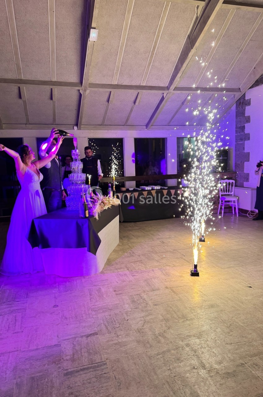 Une femme en robe blanche lève les bras près d'une fontaine de champagne et de feux d'artifice en intérieur.