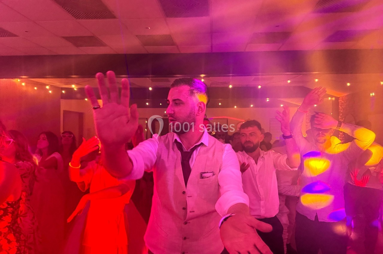 Un homme en gilet clair danse au milieu d'une foule sous des lumières colorées dans une ambiance festive.