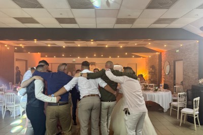Salle en pierre avec plafond en poutres apparentes, éclairages décoratifs suspendus et équipement audio-visuel installé.