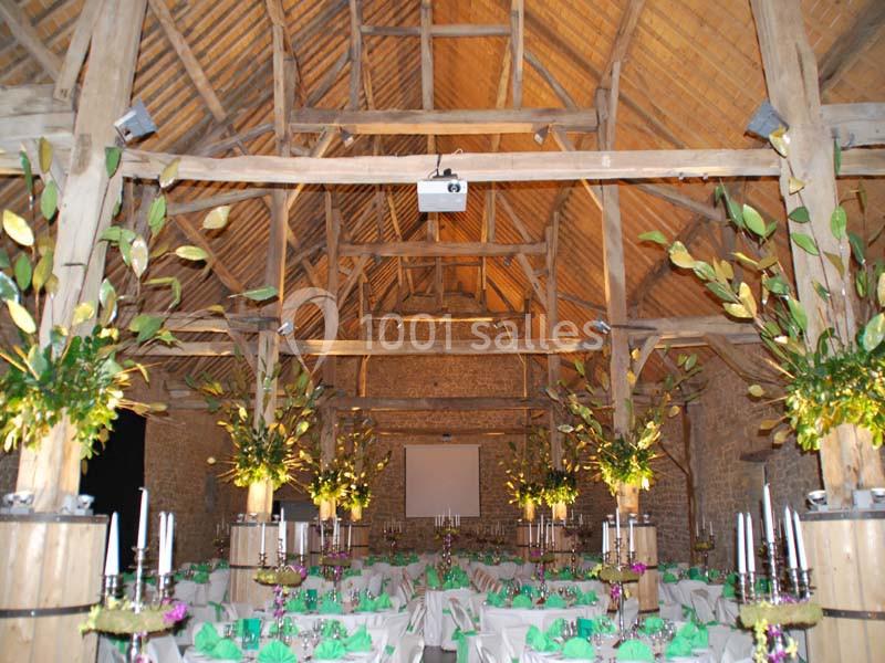 Salle de réception rustique avec charpente en bois, tables décorées de nappes vertes et arrangements floraux.