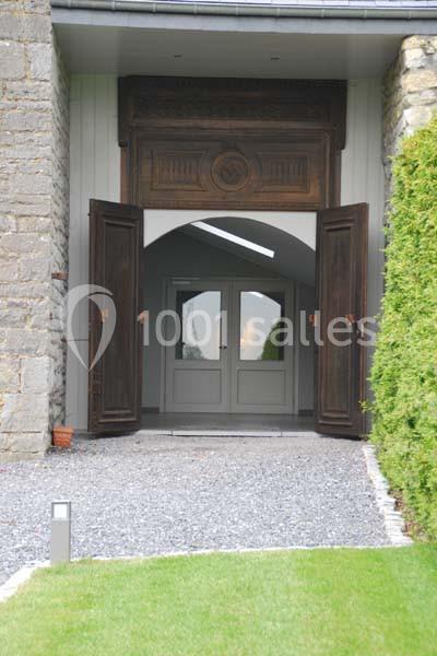 Entrée d'un bâtiment avec portes en bois ouvertes, encadrée par des murs en pierre et un chemin de gravier.
