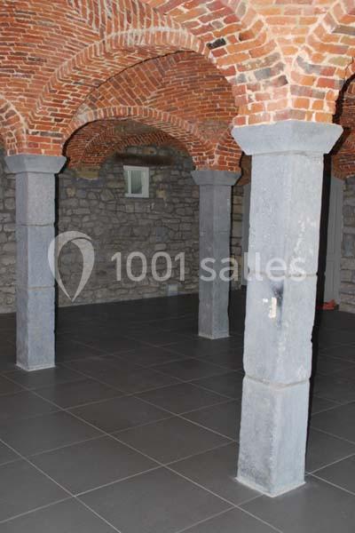 Voûtes en briques rouges soutenues par des colonnes en pierre dans une pièce au sol carrelé.