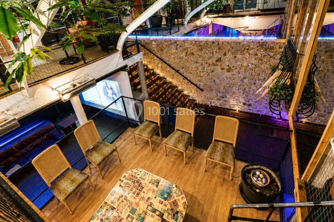 Salle avec des chaises en osier disposées autour d'une table basse, éclairage tamisé et décor végétal.