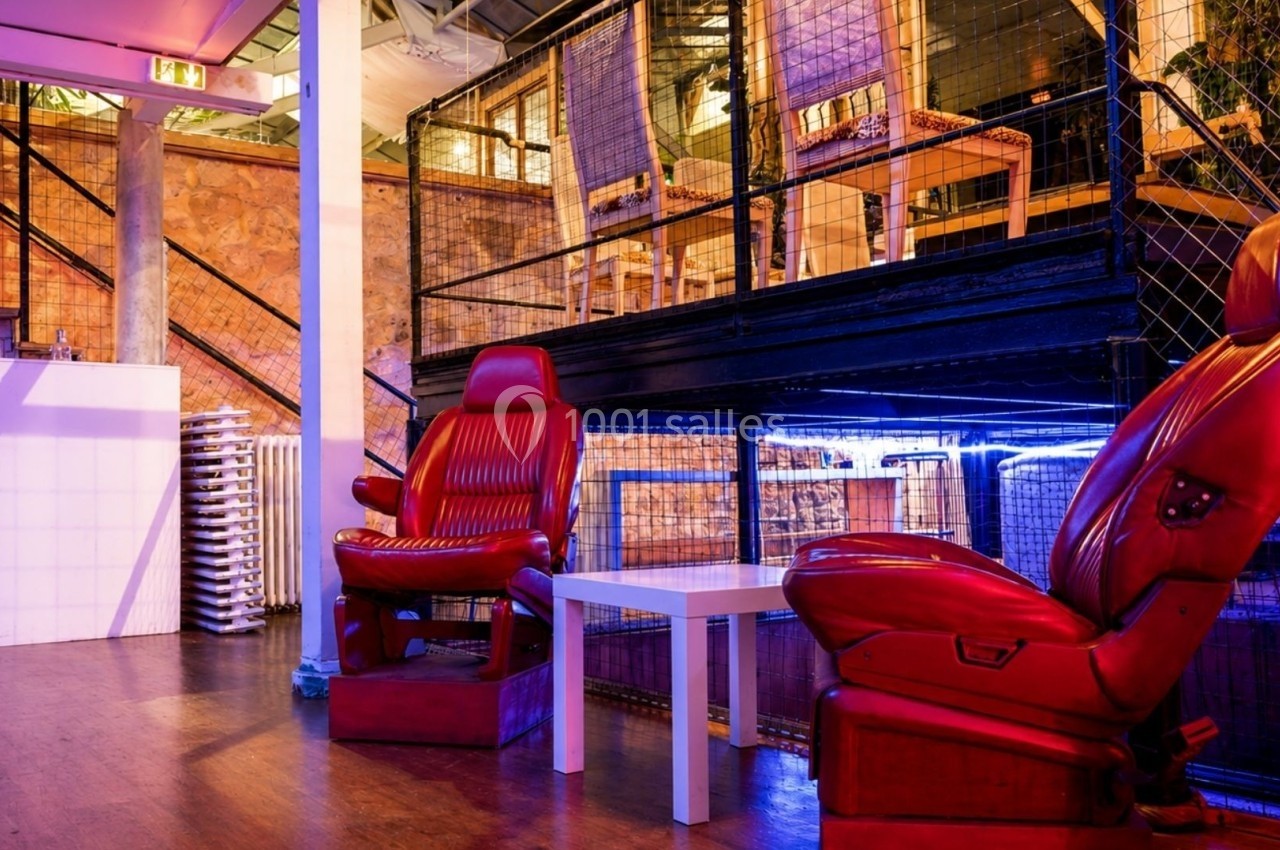 Deux fauteuils rouges devant une table basse blanche dans un espace intérieur au design industriel avec éclairage coloré.