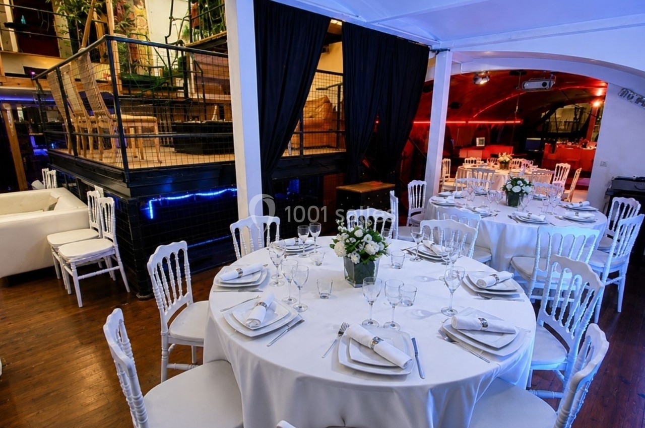 Salle de réception avec tables rondes dressées, chaises blanches et décoration élégante dans un cadre lumineux.