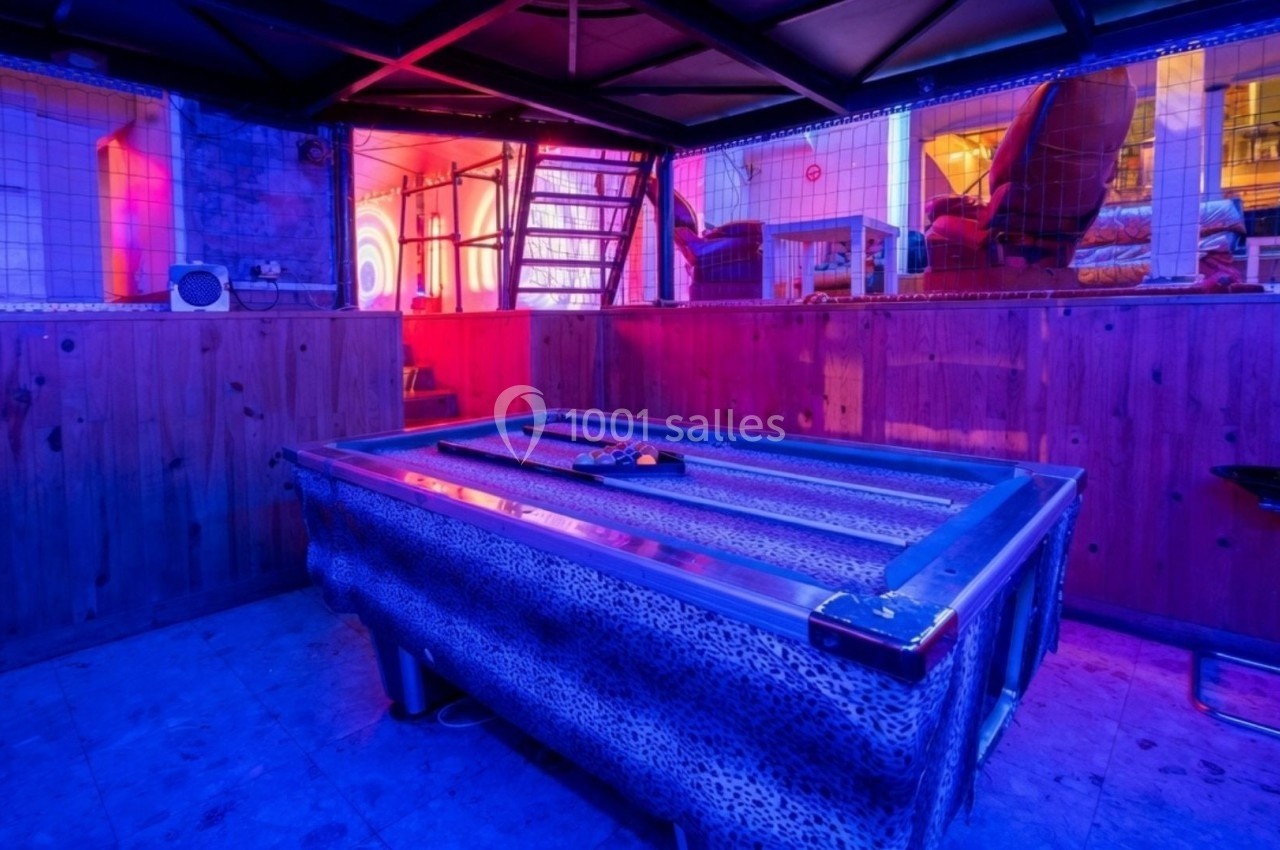 Table de billard recouverte d'un tissu à motif léopard dans une pièce éclairée par des lumières colorées.
