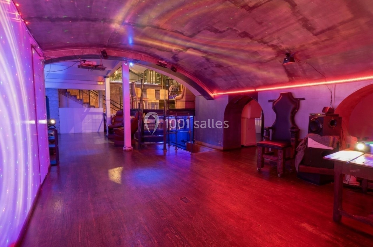 Salle voûtée avec éclairage coloré, parquet en bois, mobilier ancien et équipements audio-visuels modernes.