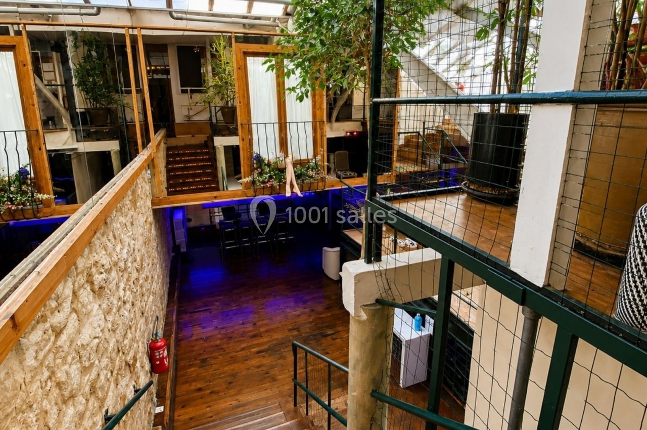 Intérieur d'un espace lumineux avec mezzanine, murs en pierre, plantes et parquet en bois.