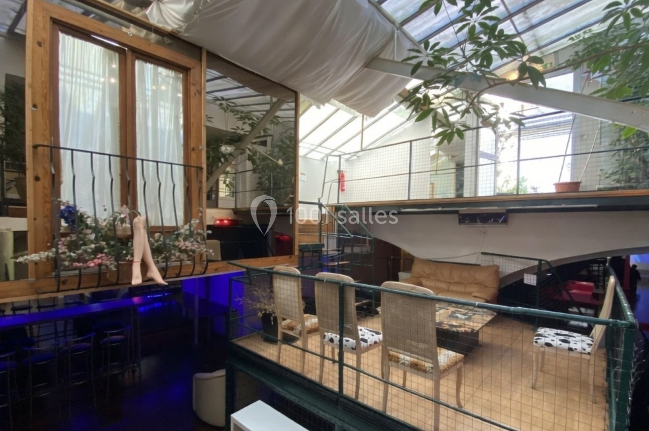 Intérieur d'un espace lumineux avec mezzanine, grandes fenêtres, plantes et mobilier moderne.
