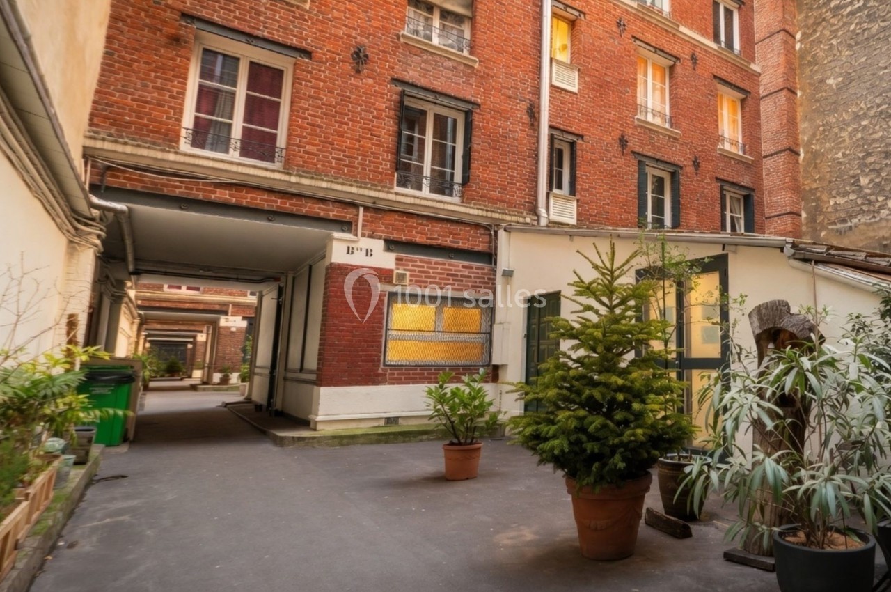 Cour intérieure d'un immeuble en briques rouges avec des plantes en pots et un passage couvert.
