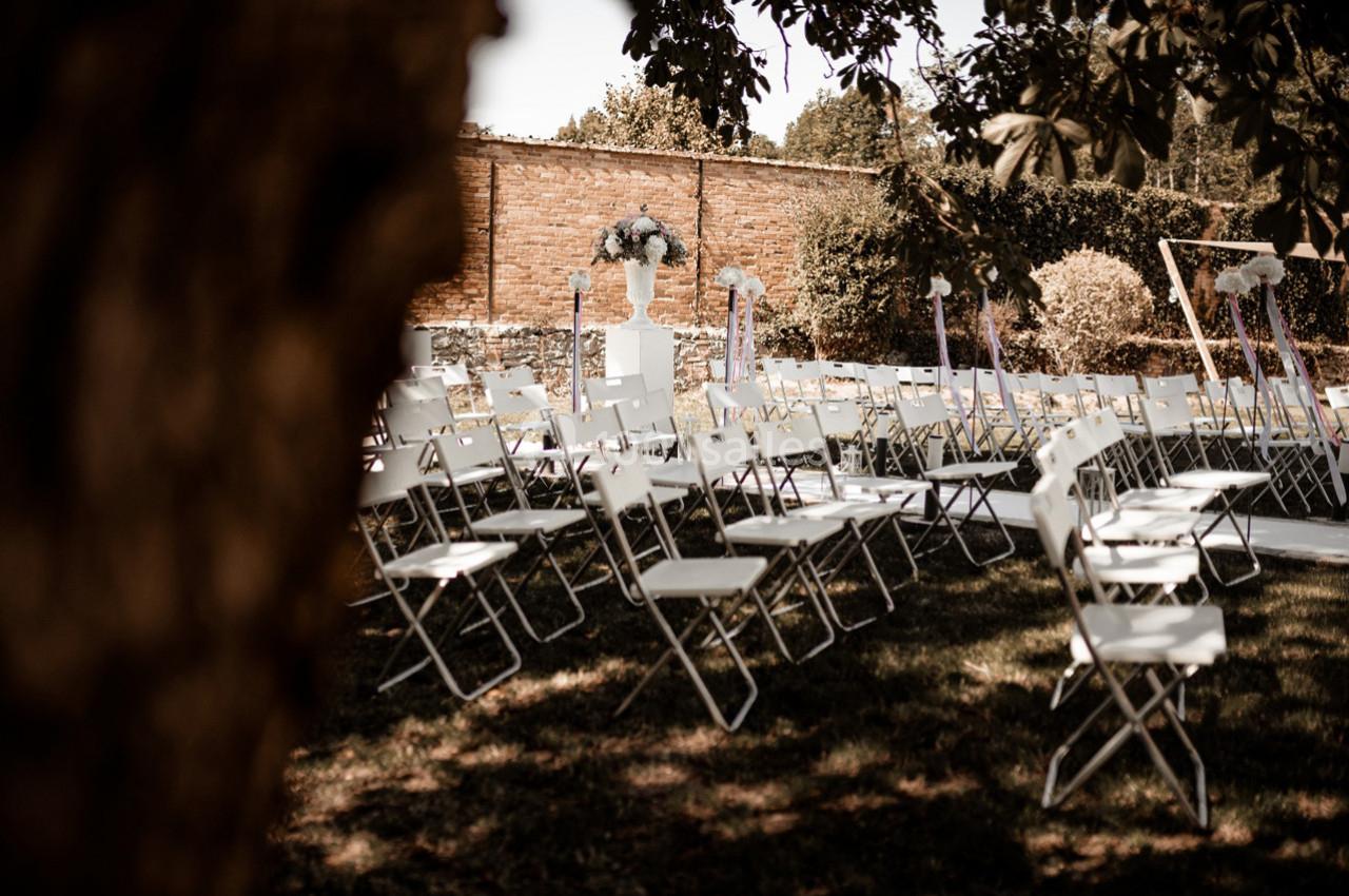 Chaises blanches disposées en rangées dans un jardin pour une cérémonie en plein air, avec un vase fleuri au centre.