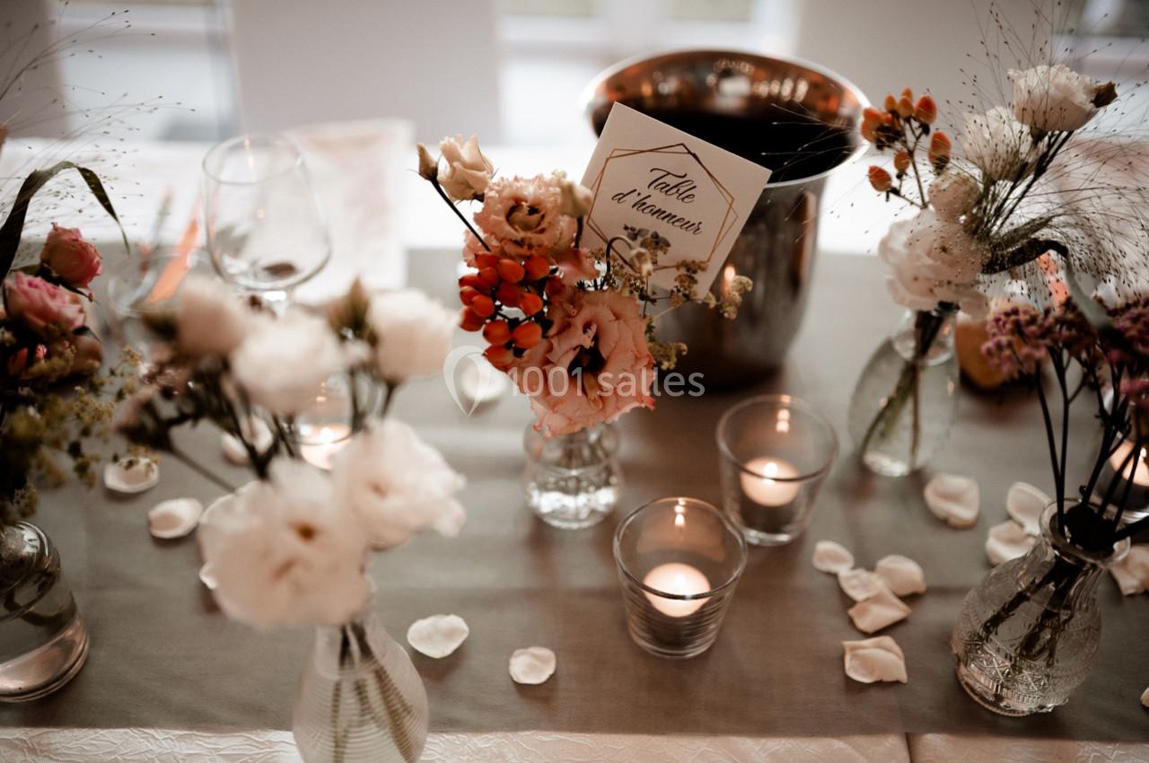 Centre de table décoratif avec fleurs, bougies allumées et une carte indiquant ’Table d'honneur’.