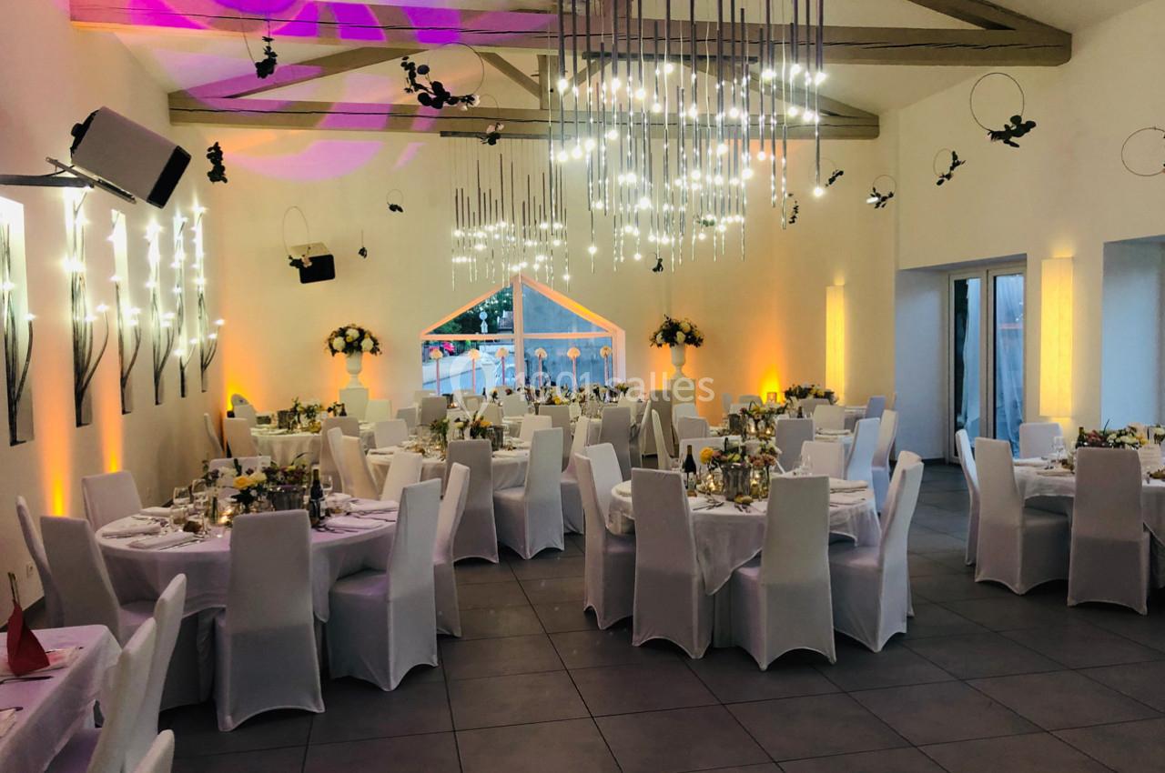 Salle de réception décorée avec des tables rondes, nappes blanches, chaises assorties et éclairage moderne.