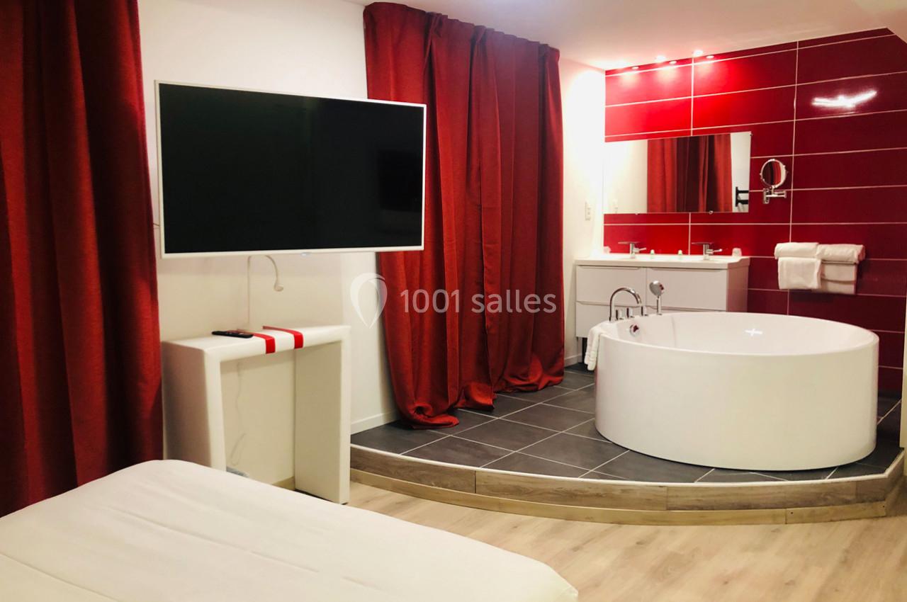 Chambre avec baignoire ronde, télévision murale, rideaux rouges et lavabo sur fond de carrelage rouge.