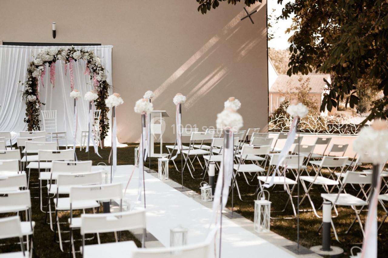 Chaises blanches alignées face à une arche fleurie dans un décor extérieur pour une cérémonie.