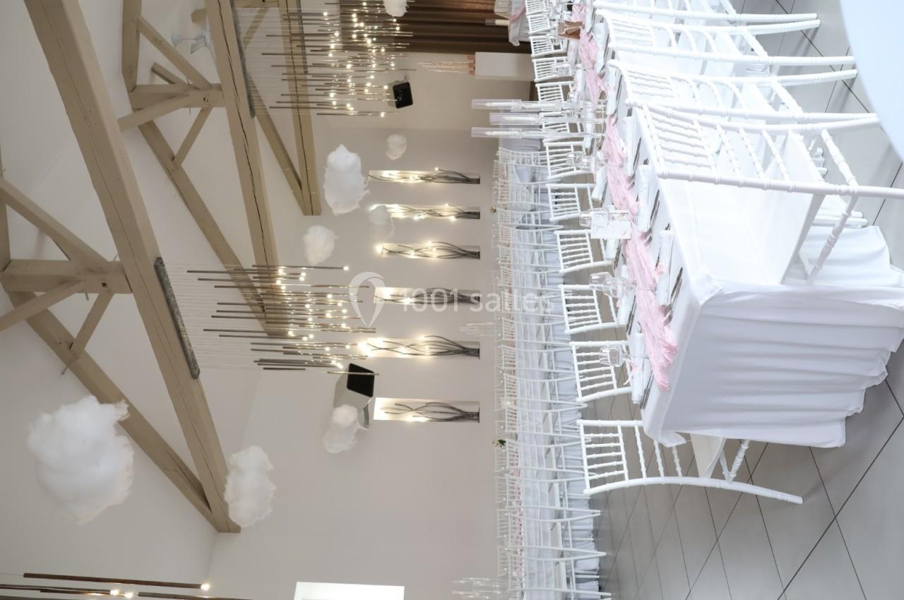 Salle de réception décorée avec des chaises blanches, nappes blanches et éléments suspendus évoquant des nuages.