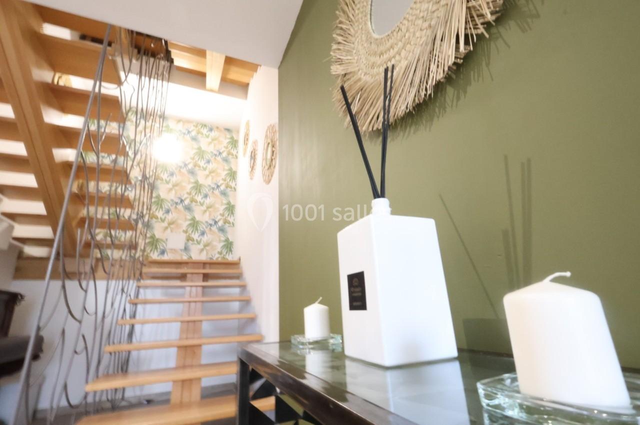 Escalier en bois avec mur vert décoré de miroirs et objets, table avec bougies et diffuseur au premier plan.