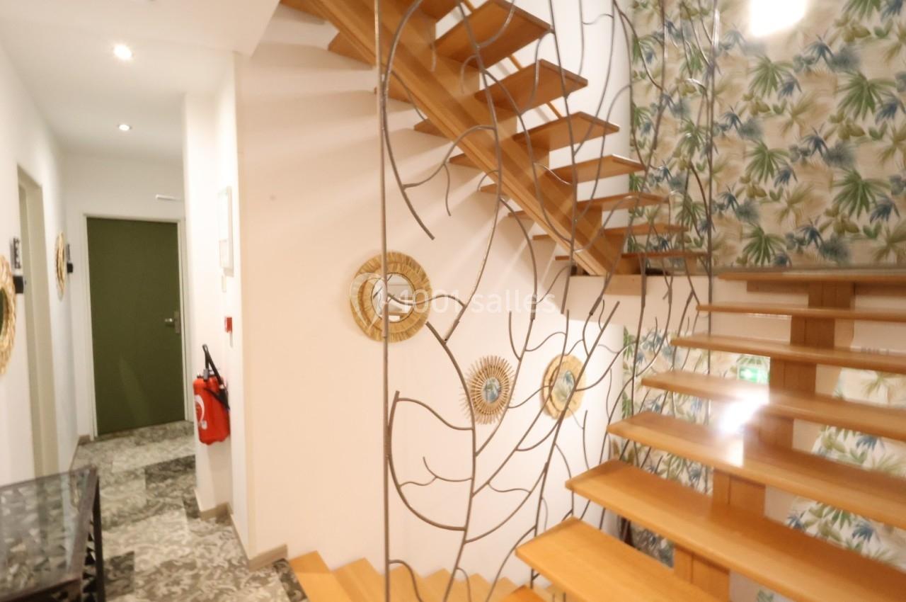 Escalier en bois avec garde-corps métallique décoratif, dans un intérieur lumineux aux murs ornés de motifs végétaux.