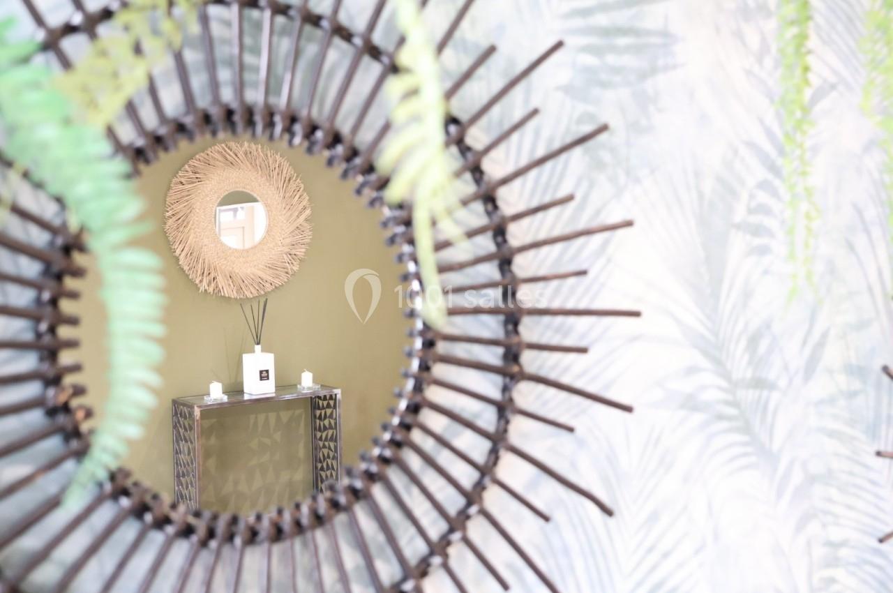 Reflet d'un miroir en rotin montrant une console avec un diffuseur de parfum et deux bougies, décorée de plantes.