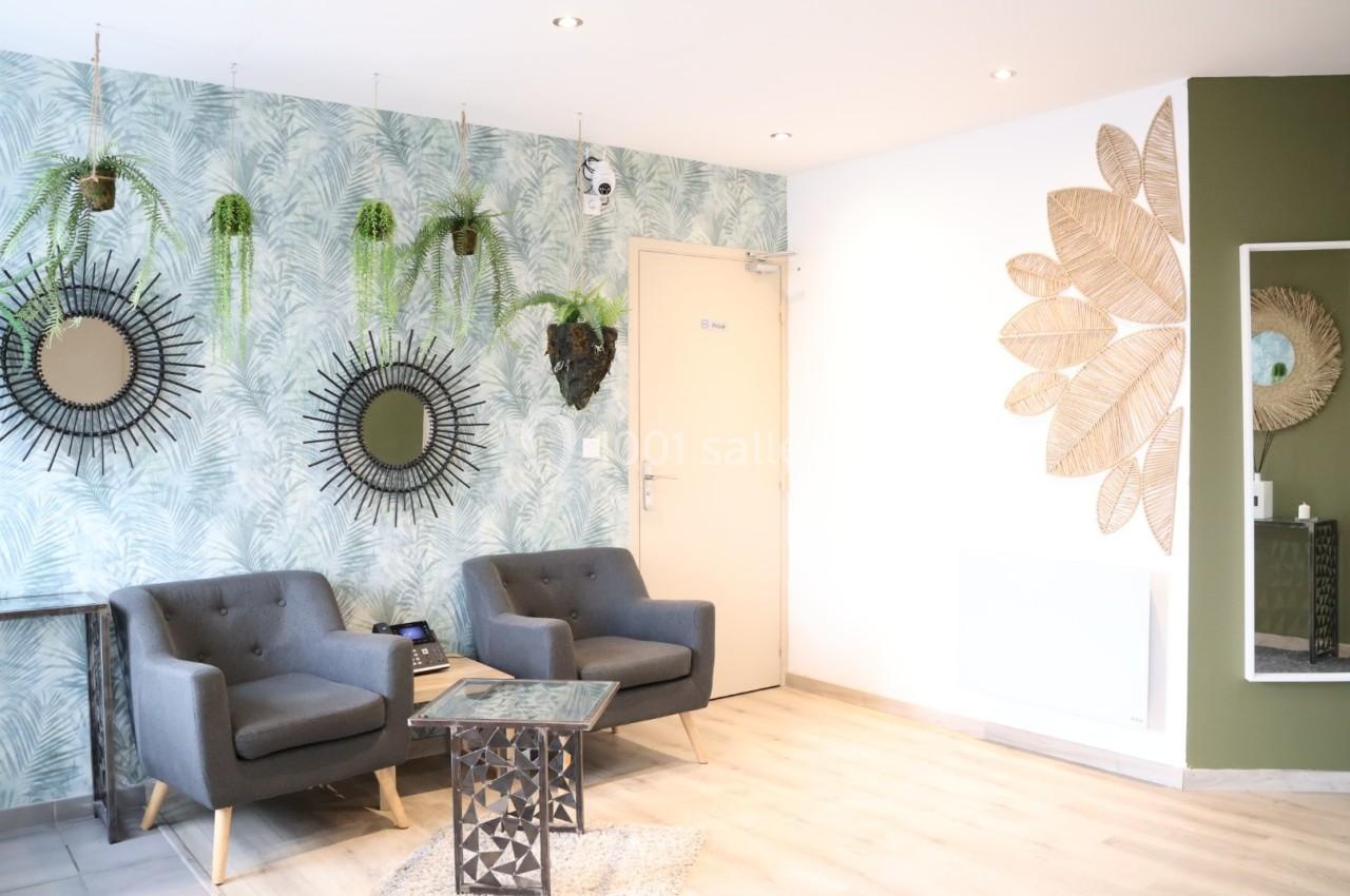 Deux fauteuils gris dans un salon lumineux, décoré de plantes suspendues, miroirs et éléments muraux naturels.