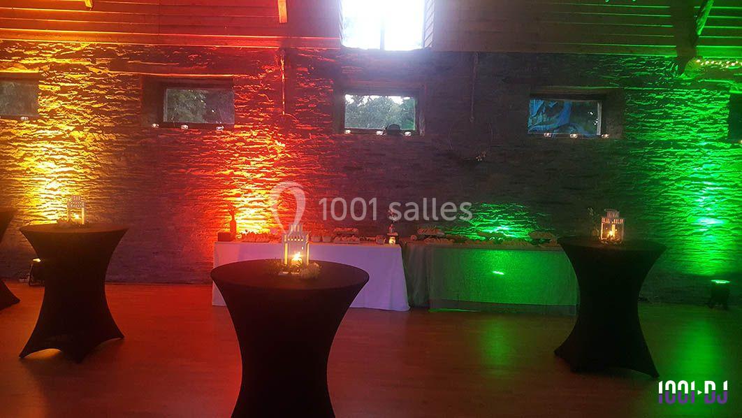 Salle décorée avec des éclairages colorés, tables hautes noires et buffet en arrière-plan.