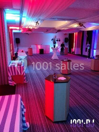 Salle de réception décorée avec des éclairages colorés, tables hautes et buffet en arrière-plan.