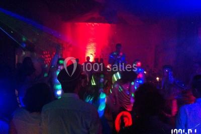 Salle de réception décorée avec des tables rondes, nappes blanches, chaises ornées de nœuds beige et éclairage vert.