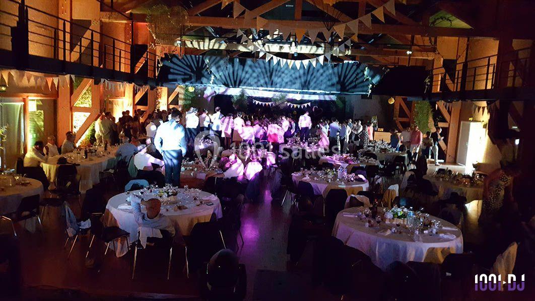 Salle de réception décorée avec des guirlandes, des tables dressées et des invités dansant sous des éclairages colorés.