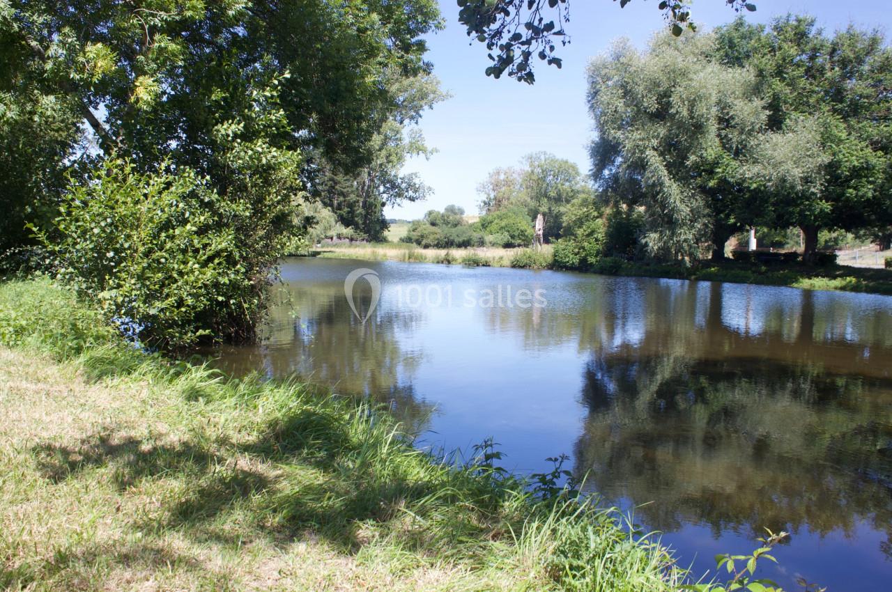 Plan d'eau calme entouré d'arbres et de végétation, reflétant le ciel bleu par une journée ensoleillée.