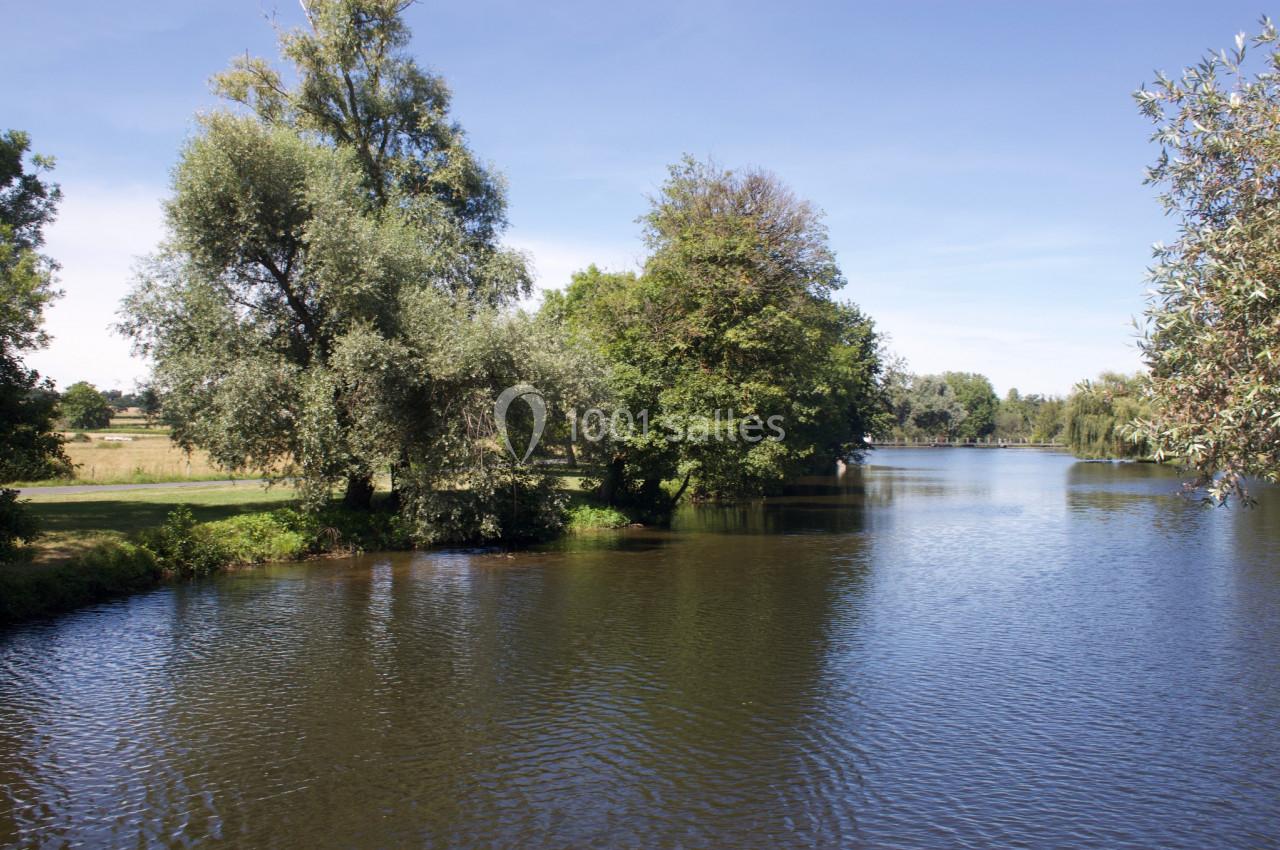 Vue d'une rivière bordée d'arbres sous un ciel bleu, avec des reflets sur l'eau calme.