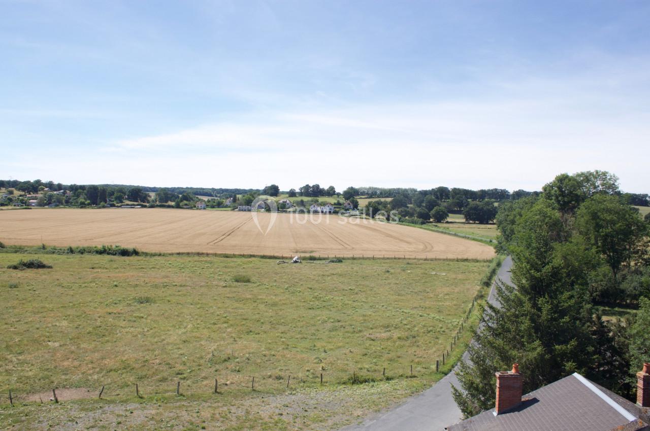 Vue d'un paysage rural avec un champ de blé, des arbres, une route sinueuse et des maisons à l'horizon.