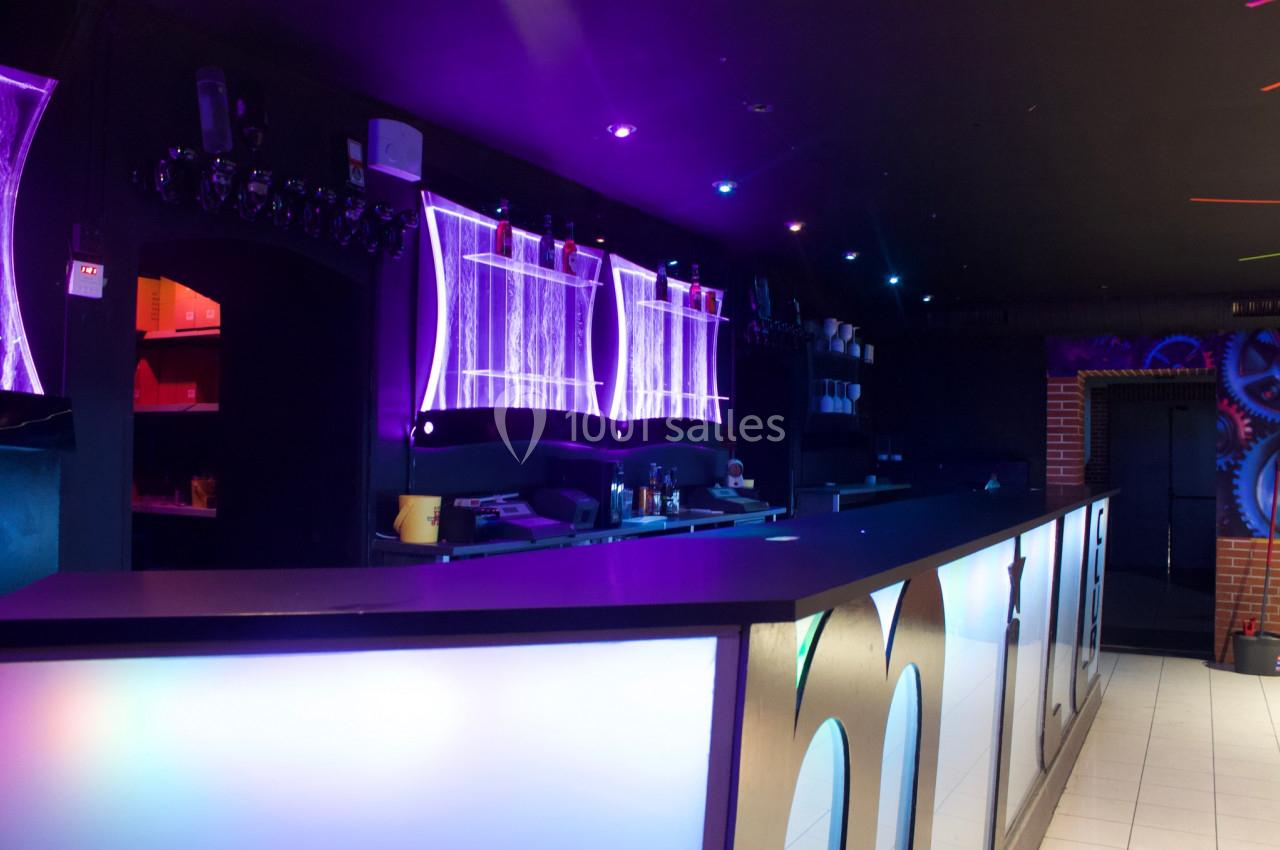 Comptoir de bar moderne éclairé par des néons violets et bleus dans une ambiance sombre.