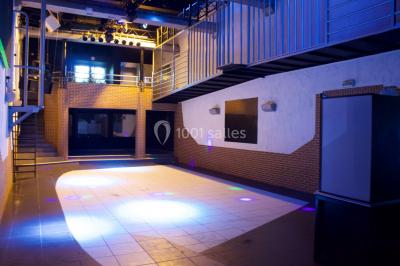 Salle de bain publique avec lavabos en inox, carrelage bleu et blanc, et portes de cabines fermées.