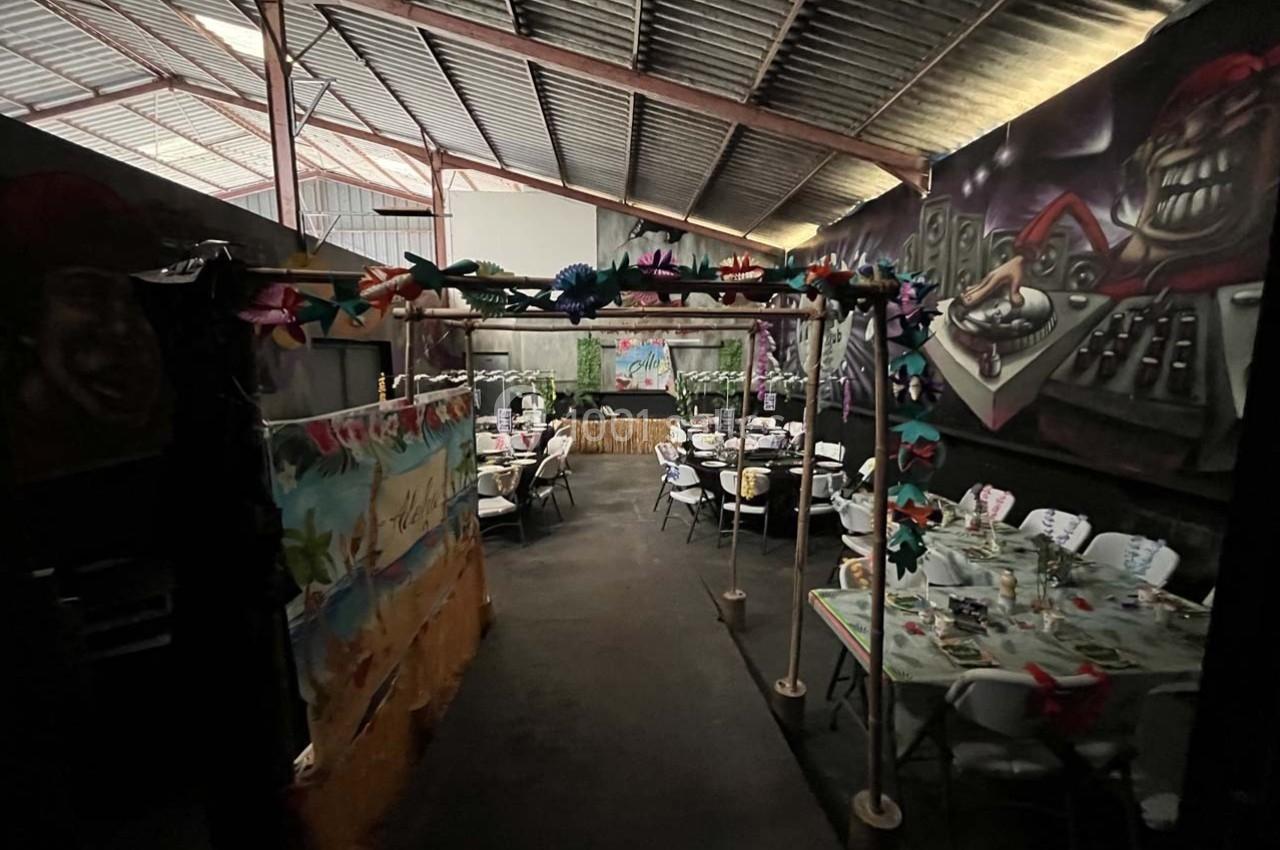 Salle décorée pour un événement avec tables dressées, guirlandes colorées et fresques murales dans un espace industriel.