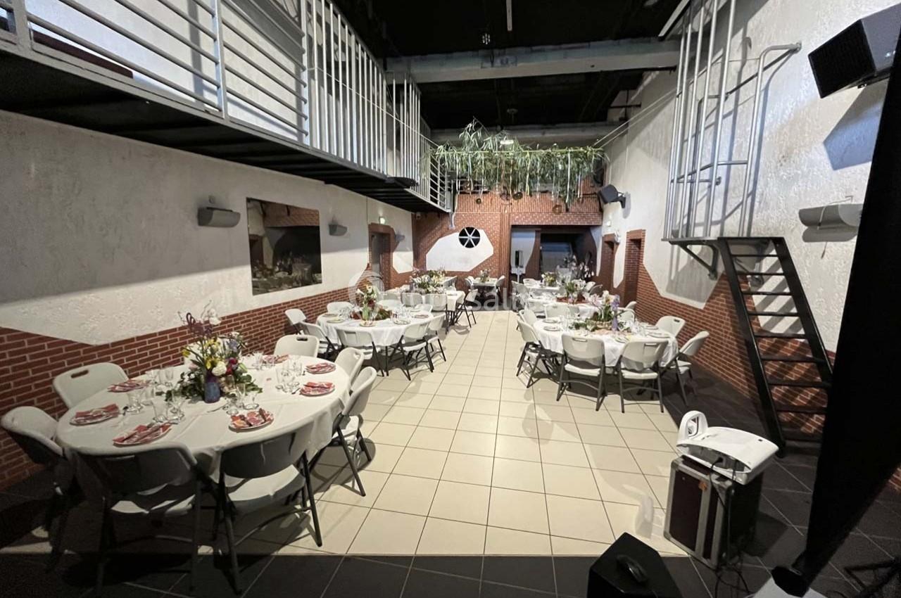 Salle de réception décorée avec des tables rondes dressées, des chaises blanches et des plantes suspendues.