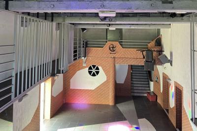 Salle de bain publique avec lavabos en inox, carrelage bleu et blanc, et portes de cabines fermées.