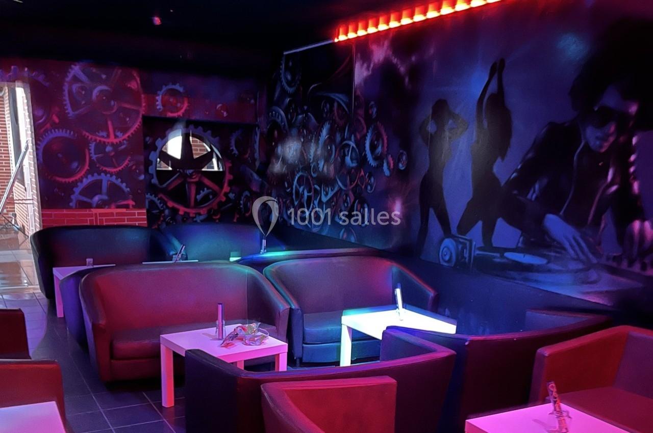 Salle sombre avec canapés rouges, tables basses blanches et mur décoré de fresques colorées sur le thème de la musique.