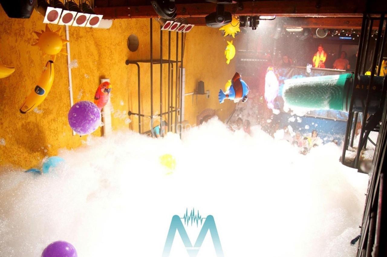 Salle de fête remplie de mousse, décorations colorées suspendues et éclairage festif.