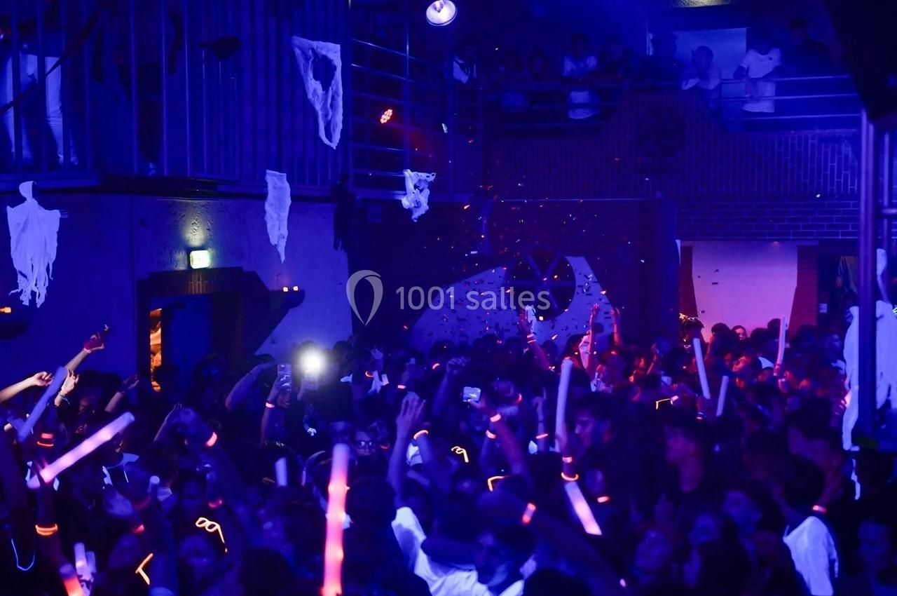 Foule dans une salle sombre décorée pour Halloween, éclairée par des lumières bleues et des accessoires lumineux.