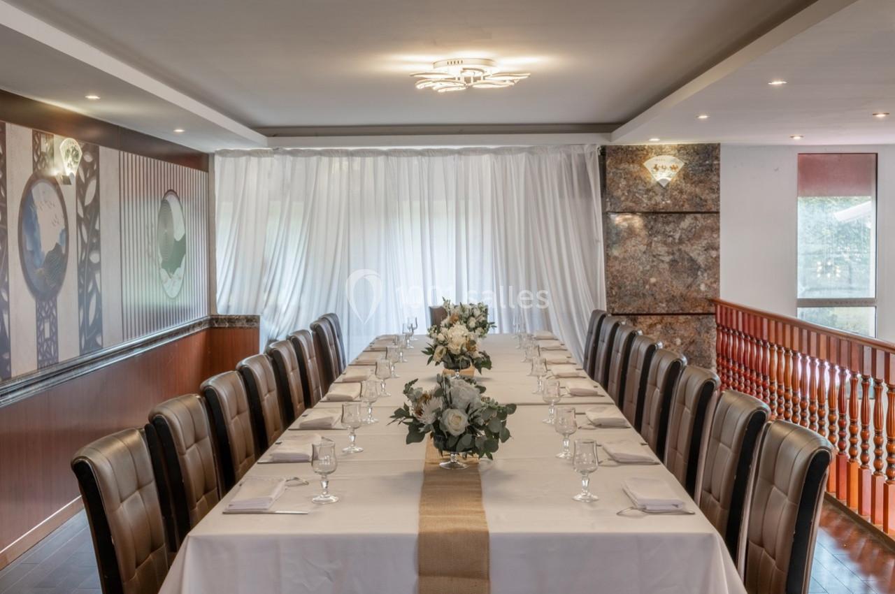 Grande table rectangulaire dressée avec une nappe blanche, décorée de fleurs et entourée de chaises en cuir brun.