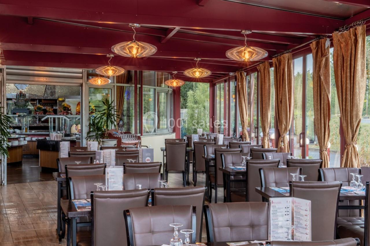 Salle de restaurant lumineuse avec tables dressées, chaises en cuir marron et grandes baies vitrées donnant sur l'extérieur.