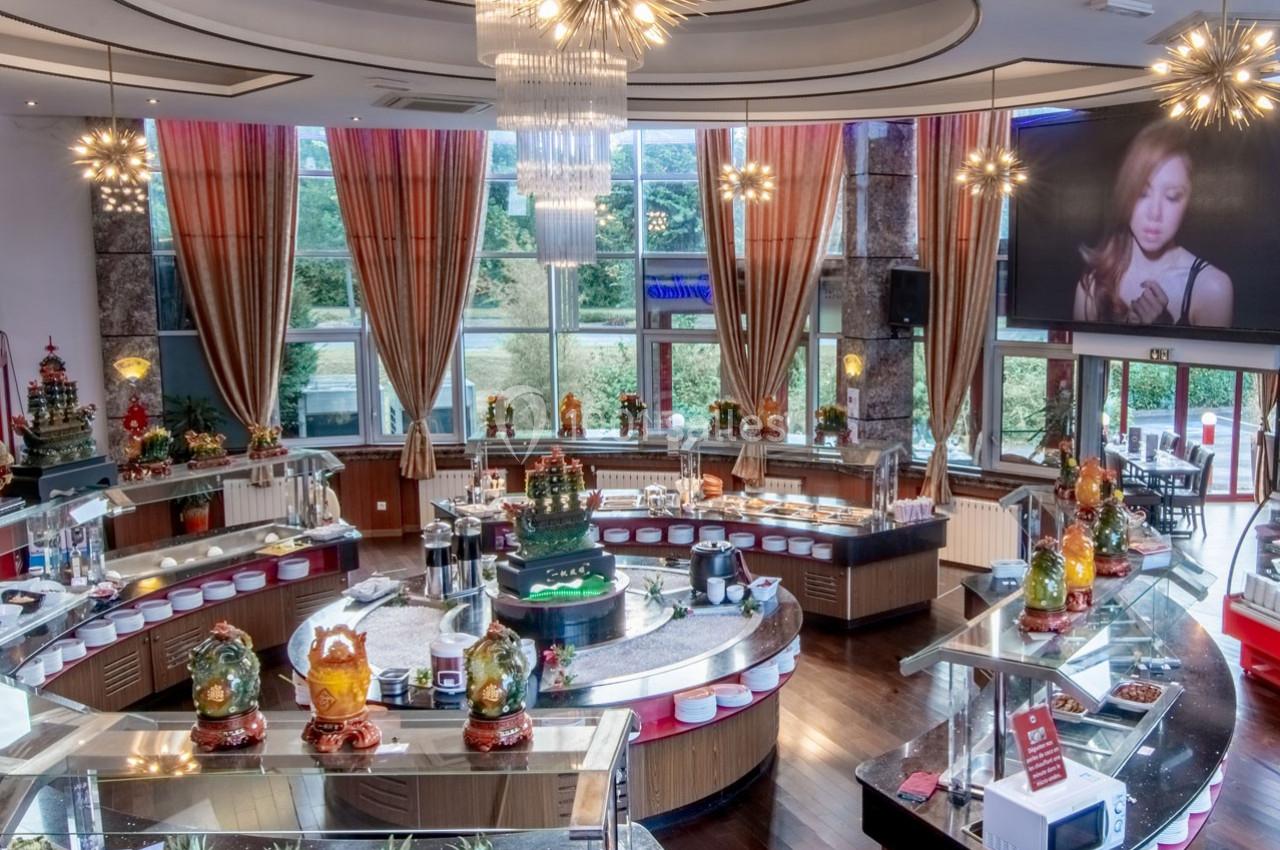 Salle de restaurant avec buffet circulaire, décorations lumineuses et grandes baies vitrées donnant sur un espace vert.