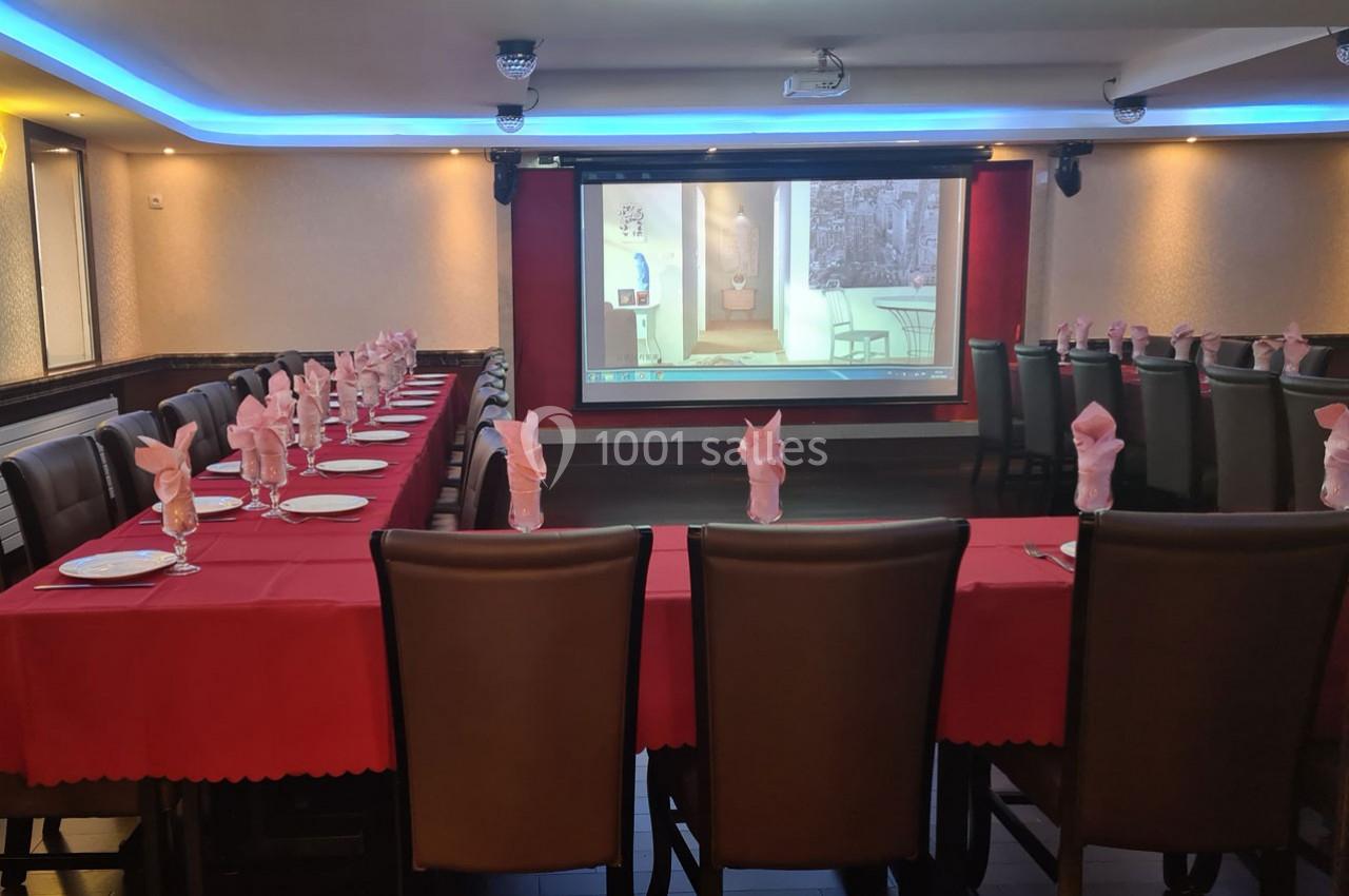 Salle de réception avec tables dressées de nappes rouges, serviettes pliées et écran de projection en arrière-plan.