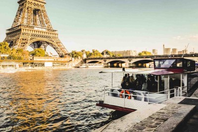 Salle de réception sur un bateau avec tables rondes dressées, nappes blanches et chaises transparentes, vue sur l'eau.