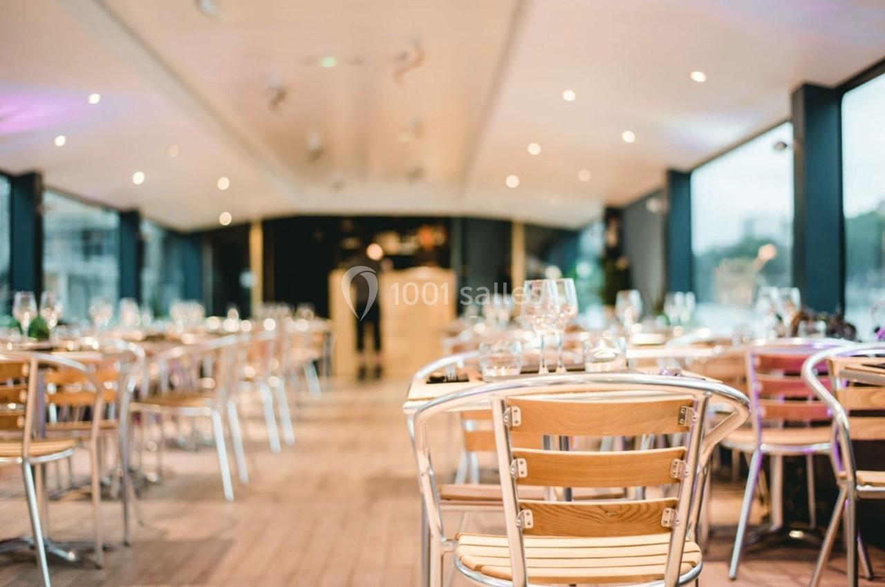 Salle de restaurant lumineuse avec des tables en bois et des chaises métalliques, vue sur de grandes baies vitrées.
