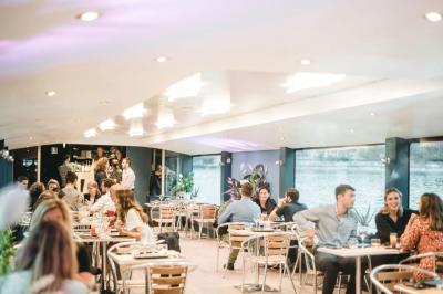 Espace extérieur d'un bateau avec fauteuils modernes, table basse, bouée de sauvetage et vue sur une rivière et un pont.