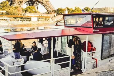 Espace extérieur d'un bateau avec fauteuils modernes, table basse, bouée de sauvetage et vue sur une rivière et un pont.