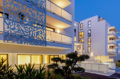 Terrasse extérieure éclairée la nuit avec des tables, des chaises longues et une vue sur une piscine illuminée.