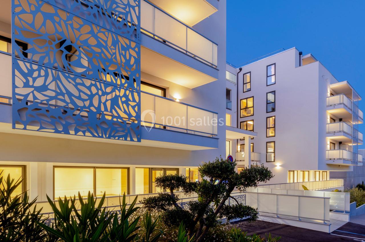 Façade moderne d'un immeuble résidentiel avec balcons éclairés et motifs décoratifs, entouré de végétation.