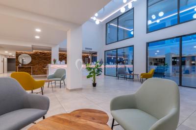 Terrasse extérieure éclairée la nuit avec des tables, des chaises longues et une vue sur une piscine illuminée.